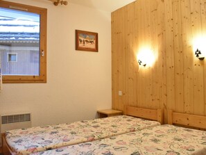 Ein Zimmer mit zwei Betten, einem Fenster, einem Wandbild und einer Wandleuchte.
