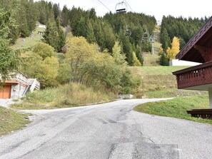 A road leading to a building with a wooden facade, a ski lift in the background, and a forested hillside. - Well-located studio - 2 guests (Méribel)