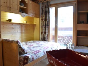 Ein Zimmer mit einem Bett, einem Holzschrank mit Regalen, einem Glastisch und Blick durch eine Tür.