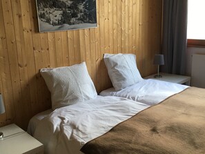 A hotel room with a wooden paneled wall, a bed with white bedding, and a nightstand with a lamp. - Apartment with balcony - 4 guests, forum view (Flaine)