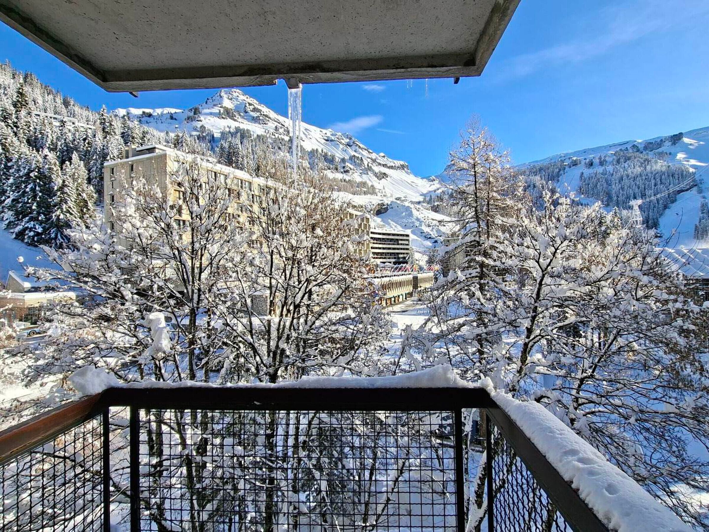 A snow-covered mountain landscape with a building and trees in the foreground.