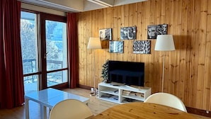 Un salon moderne avec un mur lambrissé en bois, un téléviseur à écran plat, une table basse en verre et une table à manger.
