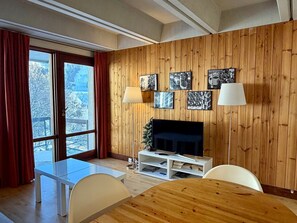 Ein modernes Wohnzimmer mit einer holzverkleideten Wand, einem Flachbildfernseher, einem Glastisch und einem Esstisch.