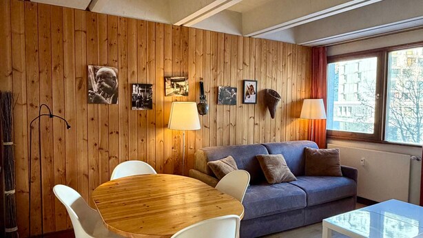 Une pièce avec un mur lambrissé en bois, un canapé, une table à manger avec des chaises et une fenêtre donnant sur des immebles.