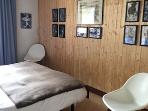 Ein Zimmer mit einem Bett, einem Sessel und einer Holzwand mit gerahmten Bildern.