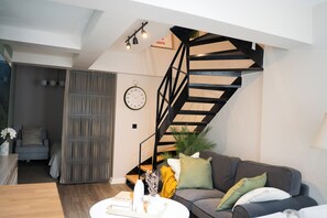 A modern living room with a staircase, a sofa, a coffee table, and a clock on the wall. - Stylish Duplex with Private Terrace near Taksim Sleeps6 Deniz Apart with cool AC (Istanbul)