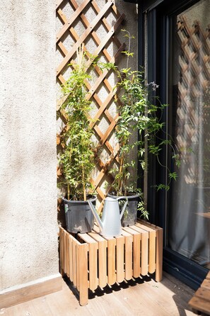 Caixa de madeira para plantas com vasos e regador em um pátio.