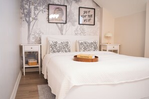 Ein Schlafzimmer mit einem Bett, zwei Nachttischen, einer Stehlampe und einer Wand mit Baum-Tapete sowie zwei gerahmten Bildern.