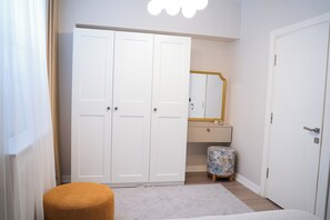 Um quarto com guarda-roupa, espelho, um banquinho pequeno e uma cama.