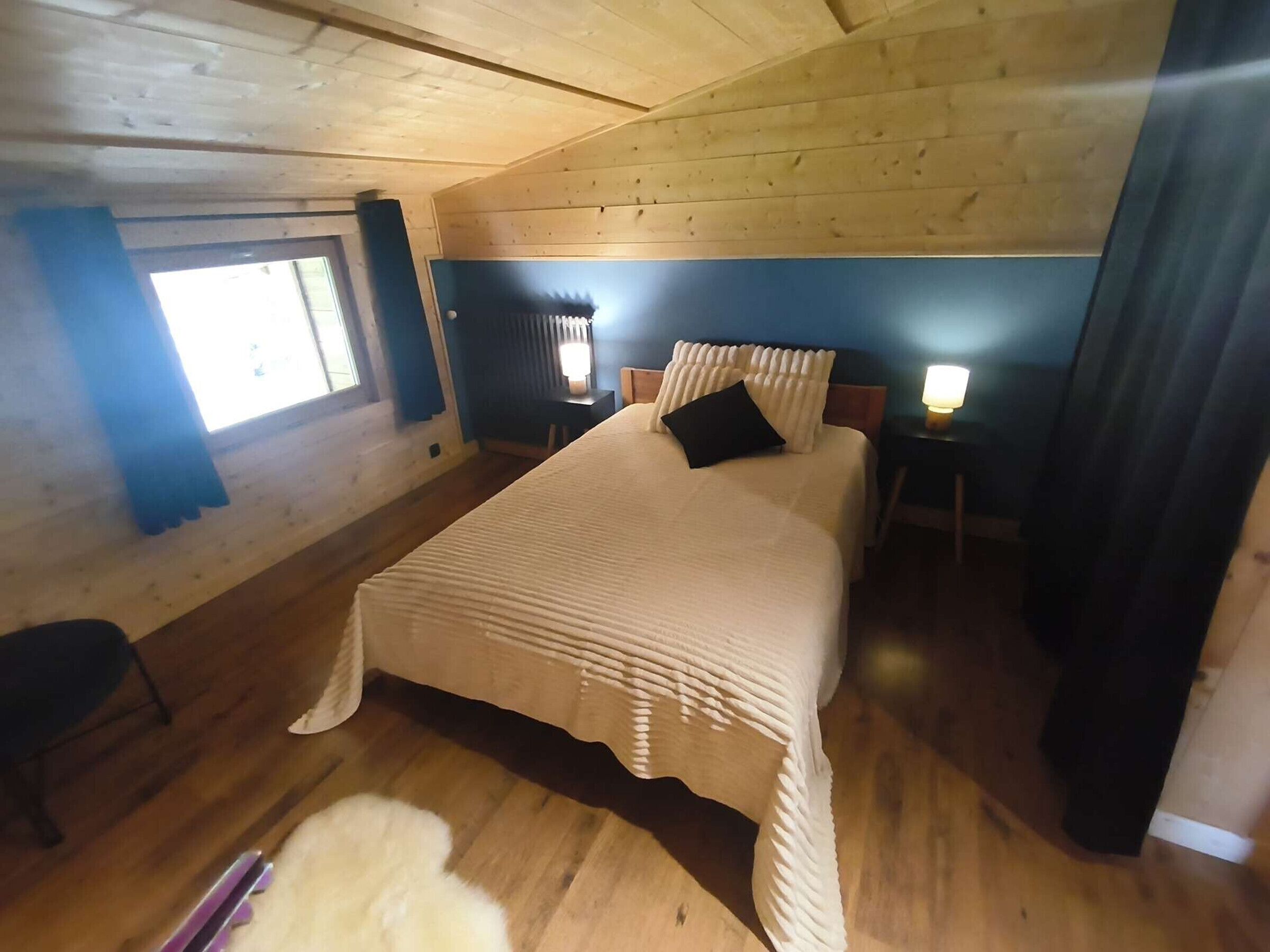 Een slaapkamer met een groot bed, houten wanden, een raam en een nachtkastje met een lamp.