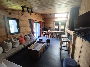 Ein Ferienhausinnenraum mit einer Couch, einem Esstisch, Stühlen, einem Fernseher und einem kleinen Hund.