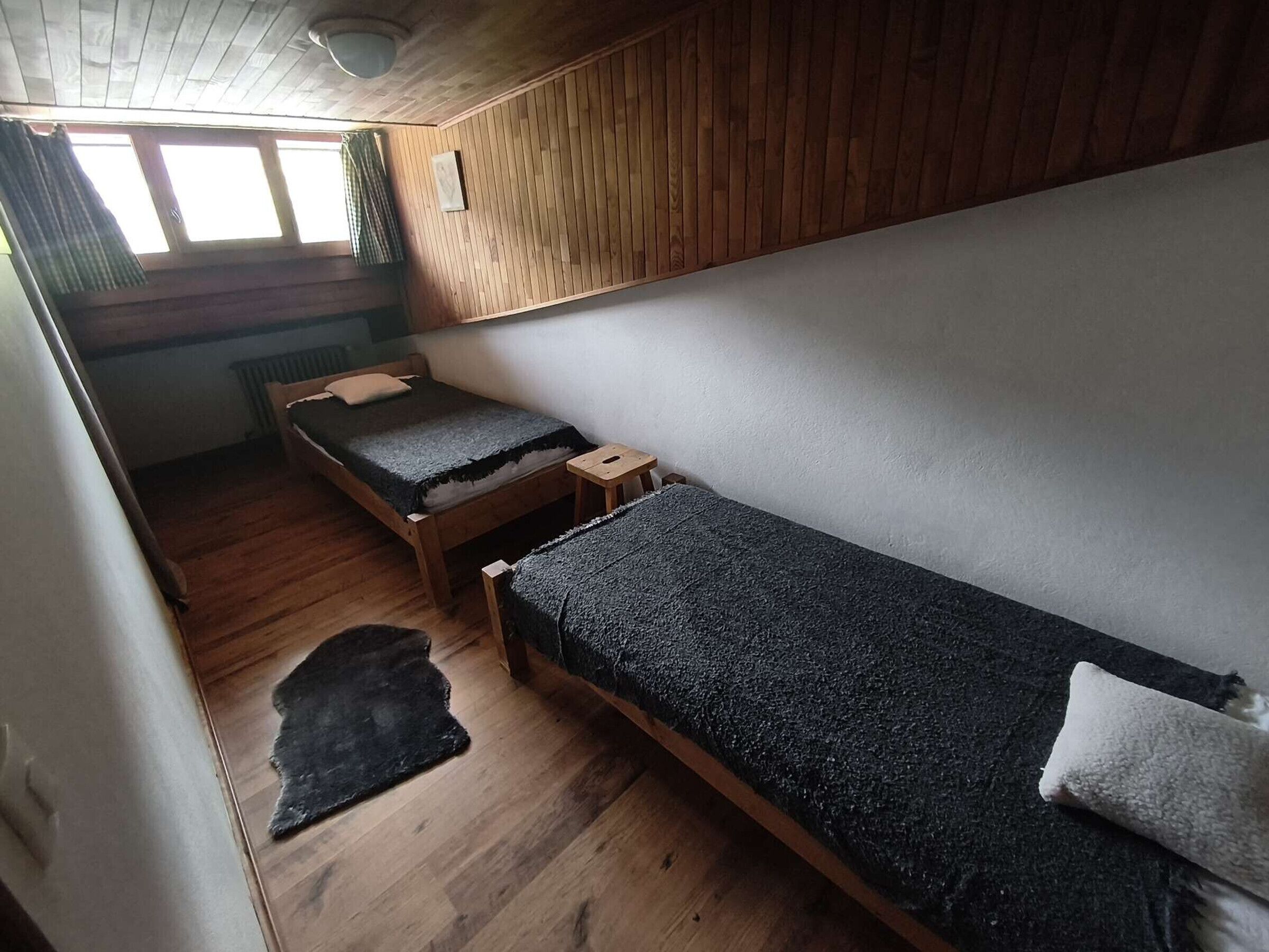 Une petite pièce, de taille modeste, avec deux lits en bois, un radiateur et une fenêtre avec des rideaux.