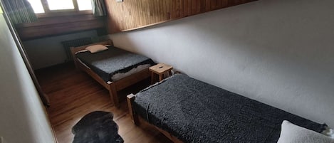 Una habitación pequeña y funcional con dos camas de madera, un radiador y una ventana con cortinas.