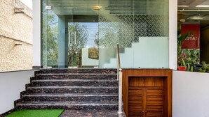 A staircase leading to a building entrance with a glass door and a wooden door, surrounded by a stone wall and a green mat. - PRISHA HOTAL AND RESTAURANTS (Zirakpur)