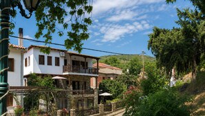 A two-story building with a balcony, surrounded by greenery and a cobblestone street. - Mountain Breeze Sanctuary with View near Volos (Alli Meria)