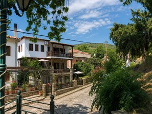 A two-story building with a balcony, surrounded by greenery and a cobblestone street. - Mountain Breeze Sanctuary with View near Volos (Alli Meria)