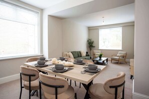 Ein Essbereich mit einem für sechs Personen gedeckten Tisch, umgeben von sechs Stühlen, in einem modernen Wohnzimmer mit einer Couch und einem Couchtisch.