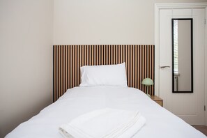 A neatly made bed with white linens and a folded towel, a bedside lamp, and a door with a mirror.