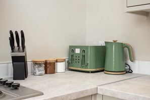 A kitchen counter with a knife block, jars, a green appliance, and a kettle.