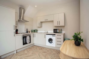 A modern kitchen with white cabinetry, a built-in oven, a microwave, and a washing machine.