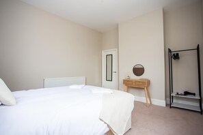 Ein Schlafzimmer mit einem Bett, einem Heizkörper, einer Tür, einem Spiegel, einem Holznachttisch und einem Kleiderständer.