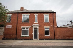Un bâtiment à deux étages, construit en briques, avec une entrée centrale, de nombreuses fenêtres et une enseigne indiquant qu’il s’agit d’une épicerie.