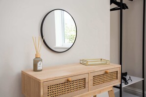 Une coiffeuse en bois, surmontée d’un miroir rond, d’un diffuseur de parfum à bâtonnets et d’un petit plateau.