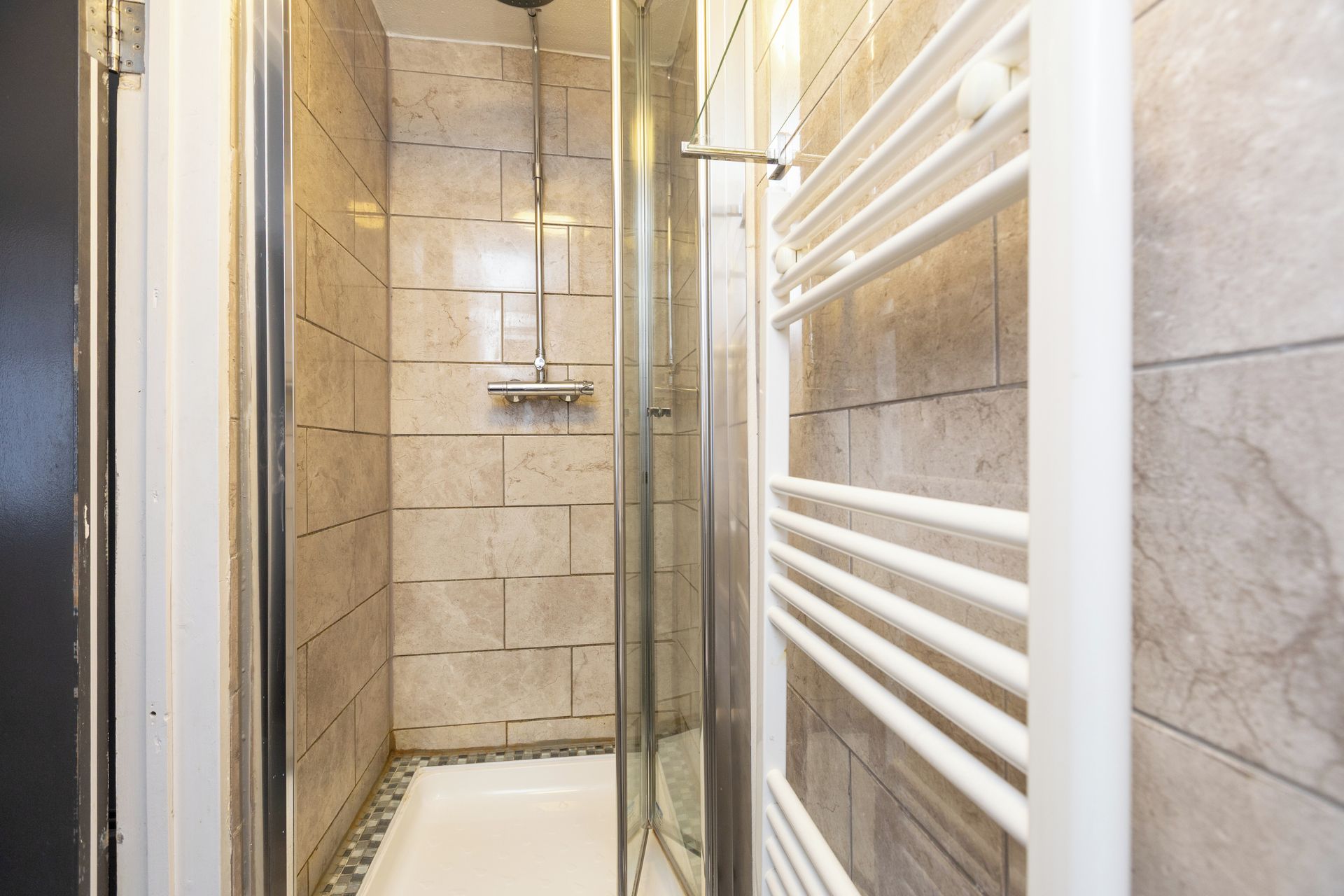A shower with a glass door, a white bathtub, and a tiled wall.