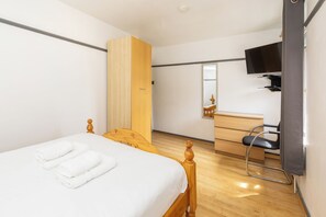 A hotel room with a bed, a wooden wardrobe, a desk with a chair, and a mounted television. - Spacious 4BDR House by Canada Water (Greater London)