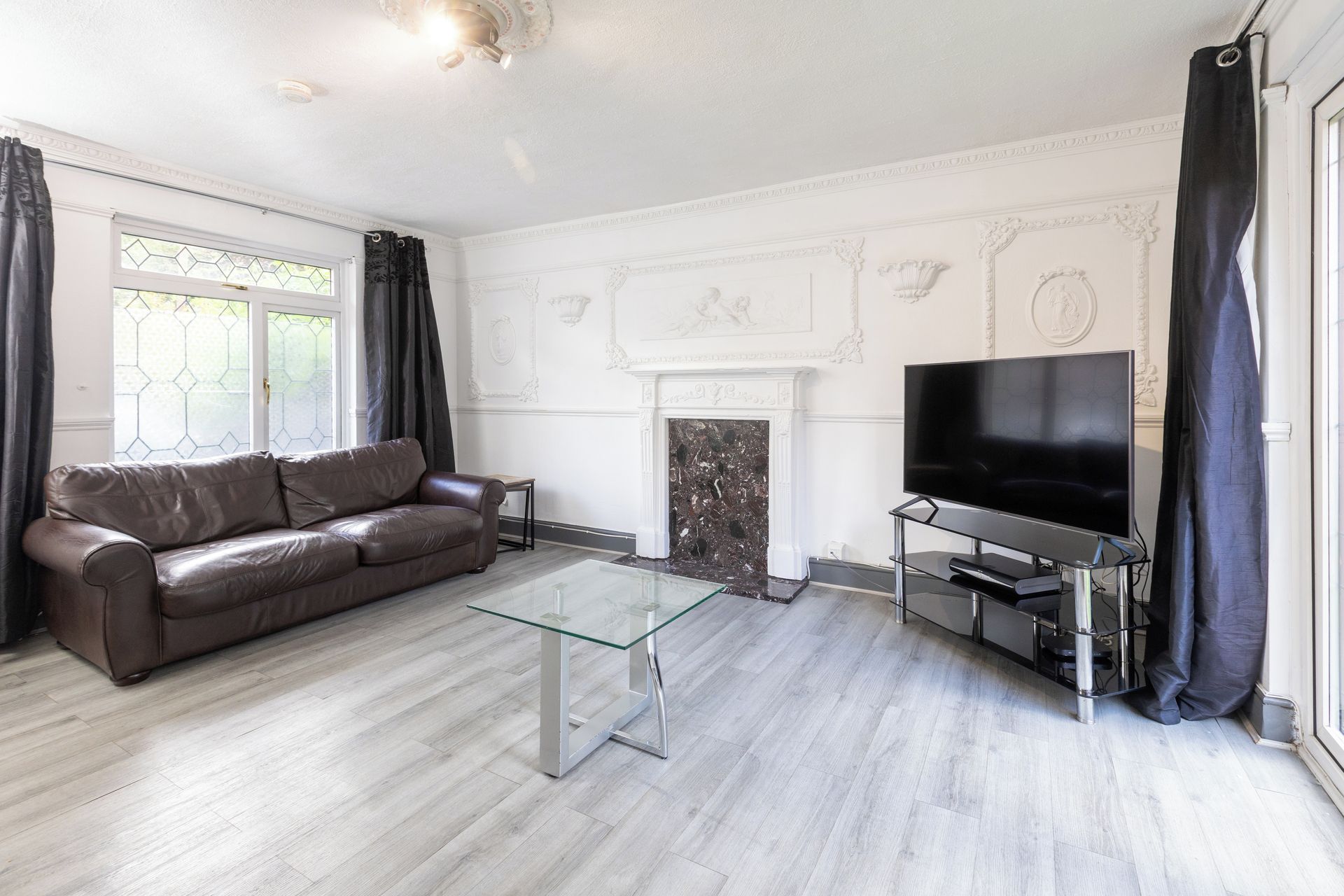 Un salon avec un canapé en cuir, une table basse en verre, un téléviseur à écran plat et une cheminée.