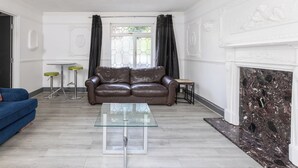 A living room with a leather sofa, a glass coffee table, a blue sofa, a fireplace, and a dining area with a table and chairs. - Spacious 4BDR House by Canada Water (Greater London)