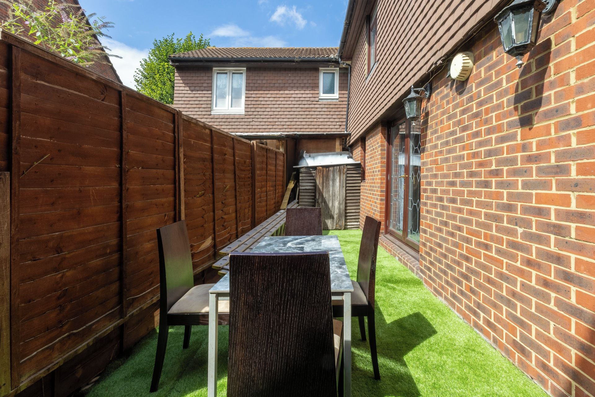 A patio area with a table and chairs, a wooden fence, and a brick wall.