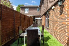A patio area with a table and chairs, a wooden fence, and a brick wall. - Spacious 4BDR House by Canada Water (Greater London)