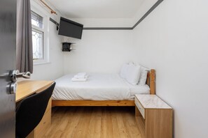 Une petite pièce propre, avec un lit en bois, un bureau et un téléviseur fixé au mur.