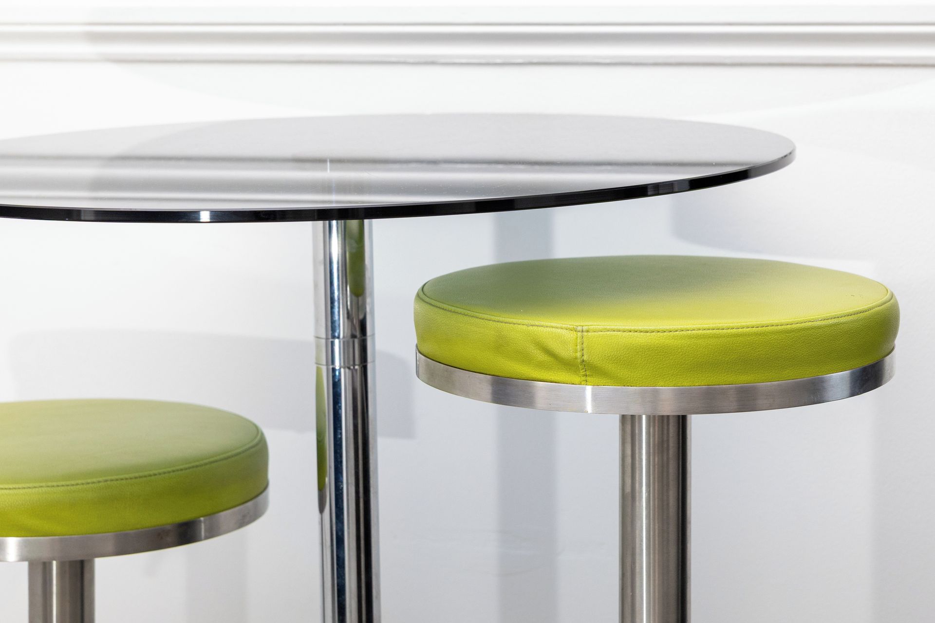 A round table with a metallic base and two green cushioned stools.