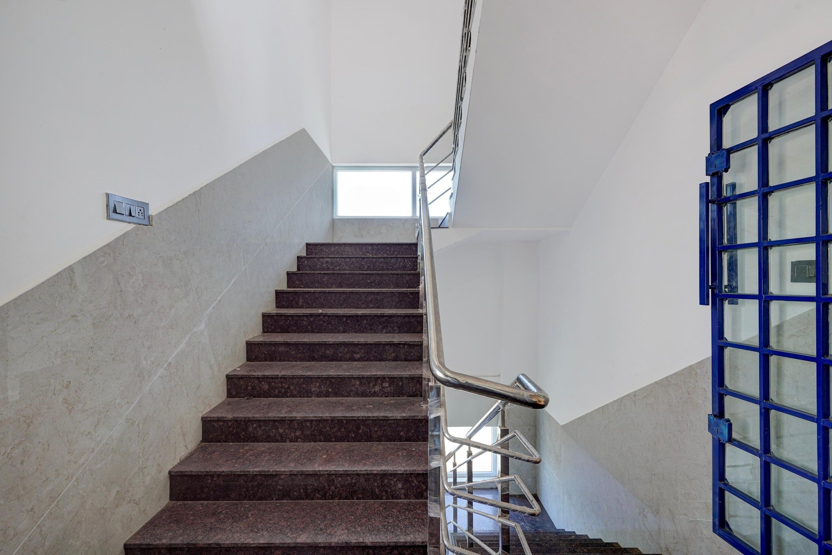 Una escalera con barandilla metálica y una puerta azul al final.