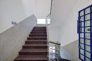 A staircase with a metal handrail and a blue door at the bottom. - Collection O Magadi Road Metro (Nelamangala)