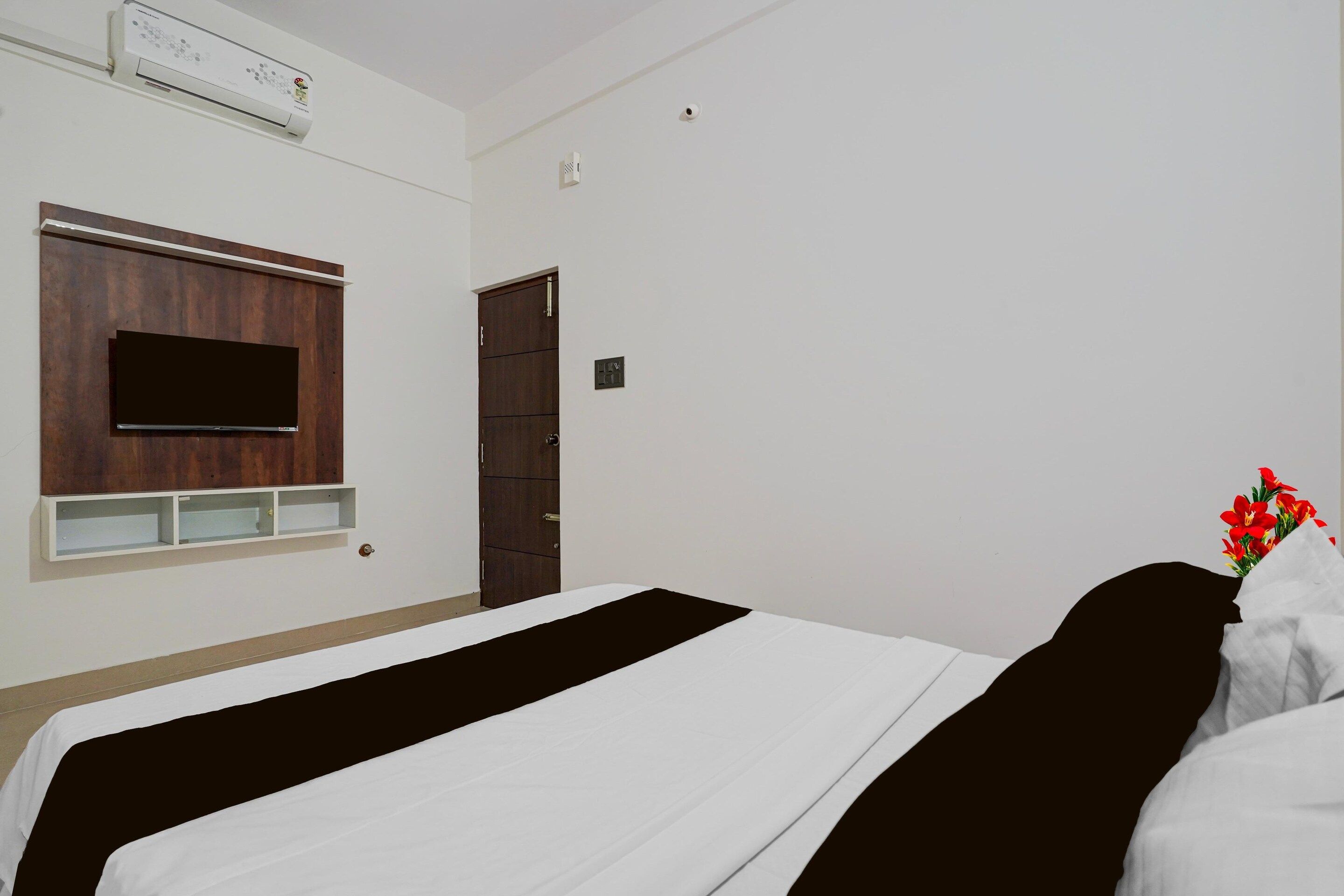 A hotel room with a bed, a TV mounted on the wall, a wooden wardrobe, and a door.