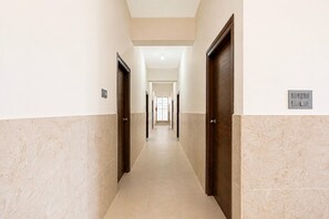 A hallway with doors on both sides, a light switch, and a window at the end. - Collection O Magadi Road Metro (Nelamangala)