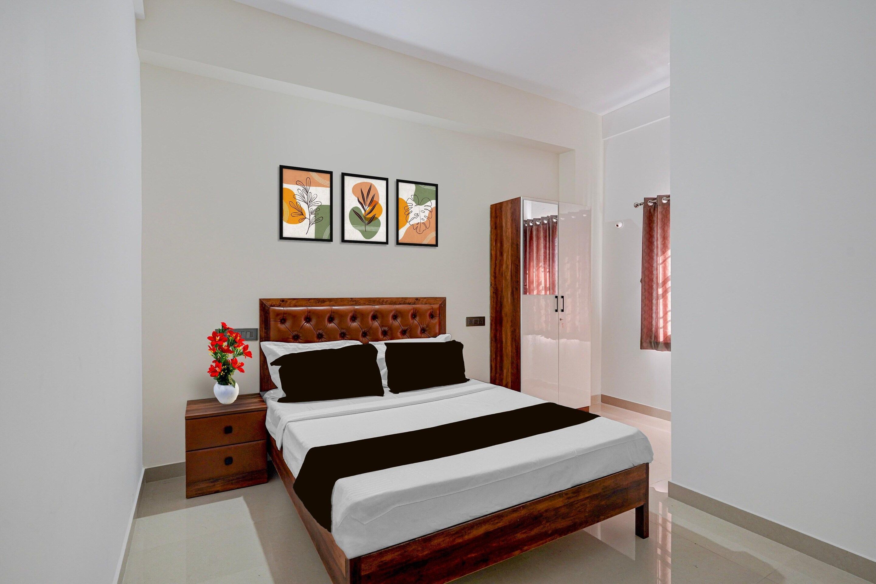 A bedroom with a bed, a nightstand, a vase of flowers, and three framed artworks on the wall.