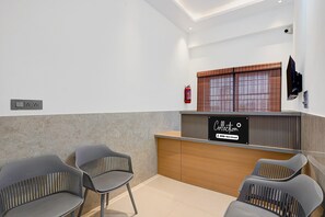 A reception area with a wooden counter, a fire extinguisher, and two grey chairs.