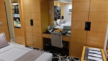 A hotel room with a bed, a desk, a mirror, and a shoe rack.