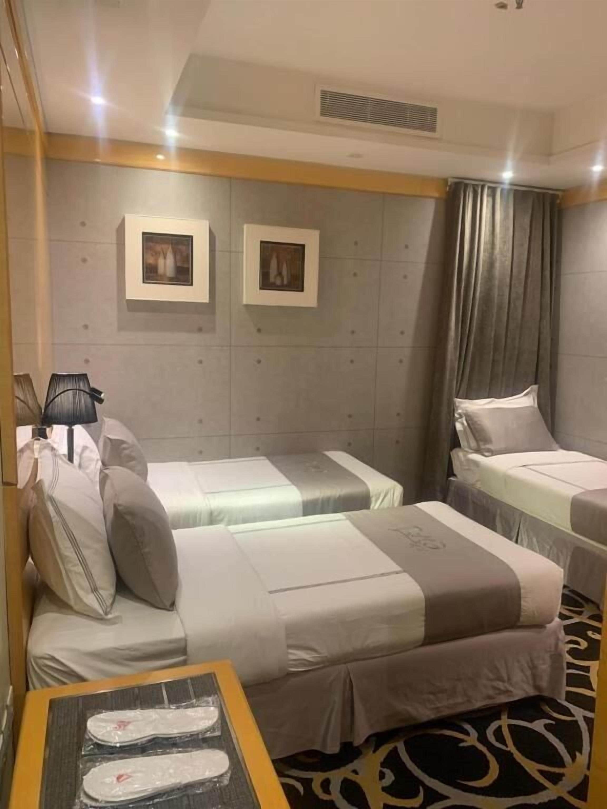 Habitación de hotel con dos camas, una mesita pequeña con pantuflas y un cuadro colgado en la pared.