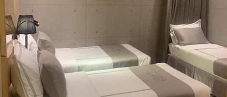 Une chambre d’hôtel avec deux lits, une petite table avec des chaussons, et un tableau accroché au mur.