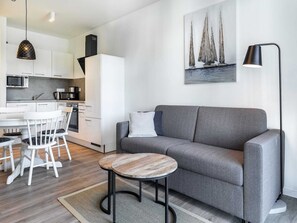 Ein zeitgemäßer Wohnraum mit grauem Sofa, rundem Couchtisch und einem Gemälde mit Segelbooten an der Wand.