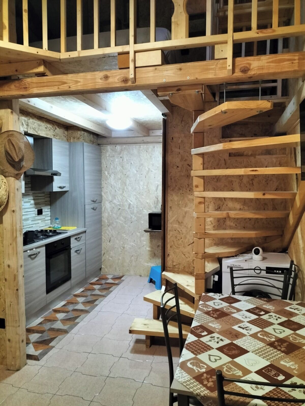 A compact kitchen with a built-in stove, a microwave, and a small refrigerator. There is a dining area with a table and chairs, and a staircase leading to an upper level.