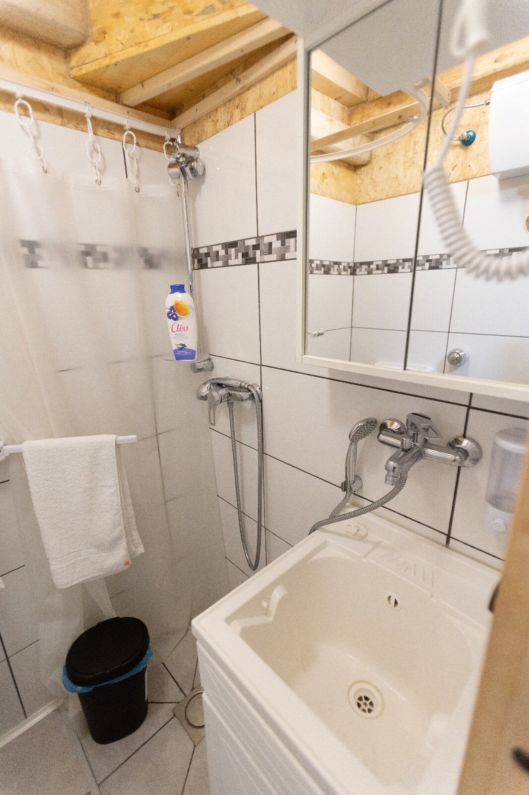 A bathroom with a shower, a sink, and a toilet. There is a towel hanging on the wall and a bottle of shampoo.
