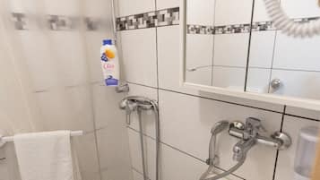 A bathroom with a shower, a sink, and a toilet. There is a towel hanging on the wall and a bottle of shampoo.