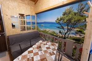 A room with a view of a beach and sea, a sofa, a table with a checkered tablecloth, and a mirror on the wall. - Stay in this romantic setting and cherish the memory for the rest of your life. (Catania)