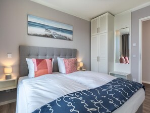 Ein Schlafzimmer mit einem Bett, Nachttischlampen, einem Kleiderschrank, einem Gemälde und einem Spiegel.